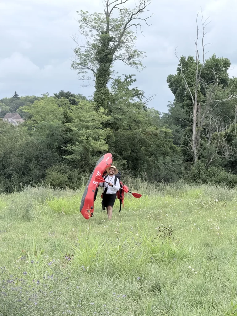 Portage d'un packraft dans les herbes, au bord du gave de Pau